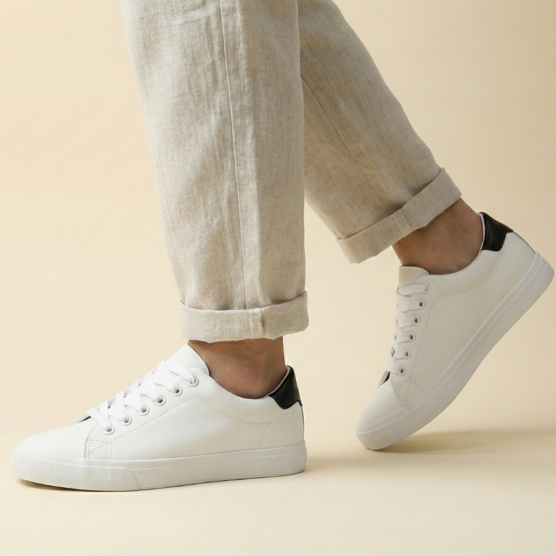 Białe sneakersy męskie z czarnymi akcentami noszone przez modela, ujęcie z przodu w ruchu, stylizacja z jasnymi spodniami.