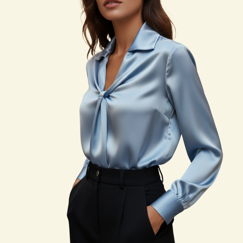 Modelka w bluzce w odcieniu niebieskiego mglistego, z delikatnym połyskiem i skręconym przodem; elegancka stylizacja biurowa.