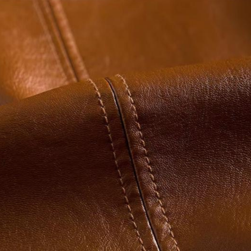 Zbliżenie na brązową skórzaną marynarkę, ukazujące naturalną strukturę skóry i precyzyjne przeszycia wzdłuż linii materiału.