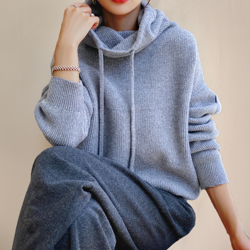 Niebieskoszary sweter oversize damski z kapturem ujęty pod kątem, z podniesioną ręką przy twarzy — Lubomirske